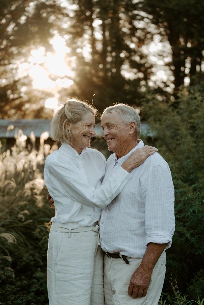 Senior couple embraces and smiles at sunset in a sunlit garden setting.